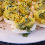 Avocado deviled eggs topped with chives and cayenne on a white plate, Healthy avocado-filled eggs with Greek yogurt and jalapeños, YMCA high-protein snack idea with avocado and eggs